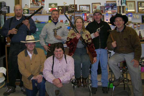Group shot of Jake Mountain, Dead Head, Jimmy Spurs holding one of those new-fangled autoloading pistols, Smokey Sue, Wild Sage, Spinter Jack and Brett Cantrell at a get-together at Jimmy Spurs workshop after the April White Mountain Regulators Shoot at Candia, NH that Jimmy Spurs won and all these shooters shot firearms worked on by him.